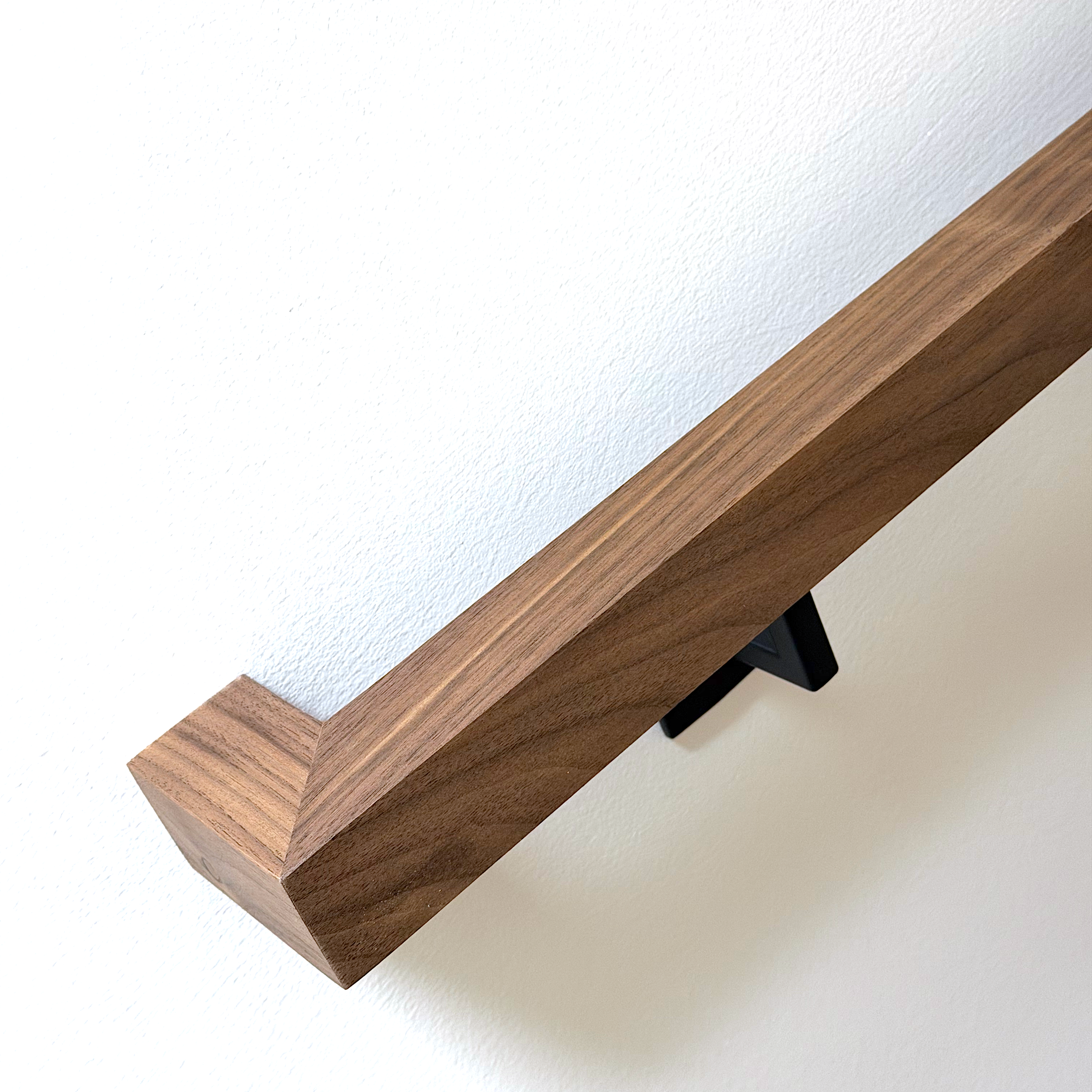Dark walnut handrail installed on wall with black square bracket